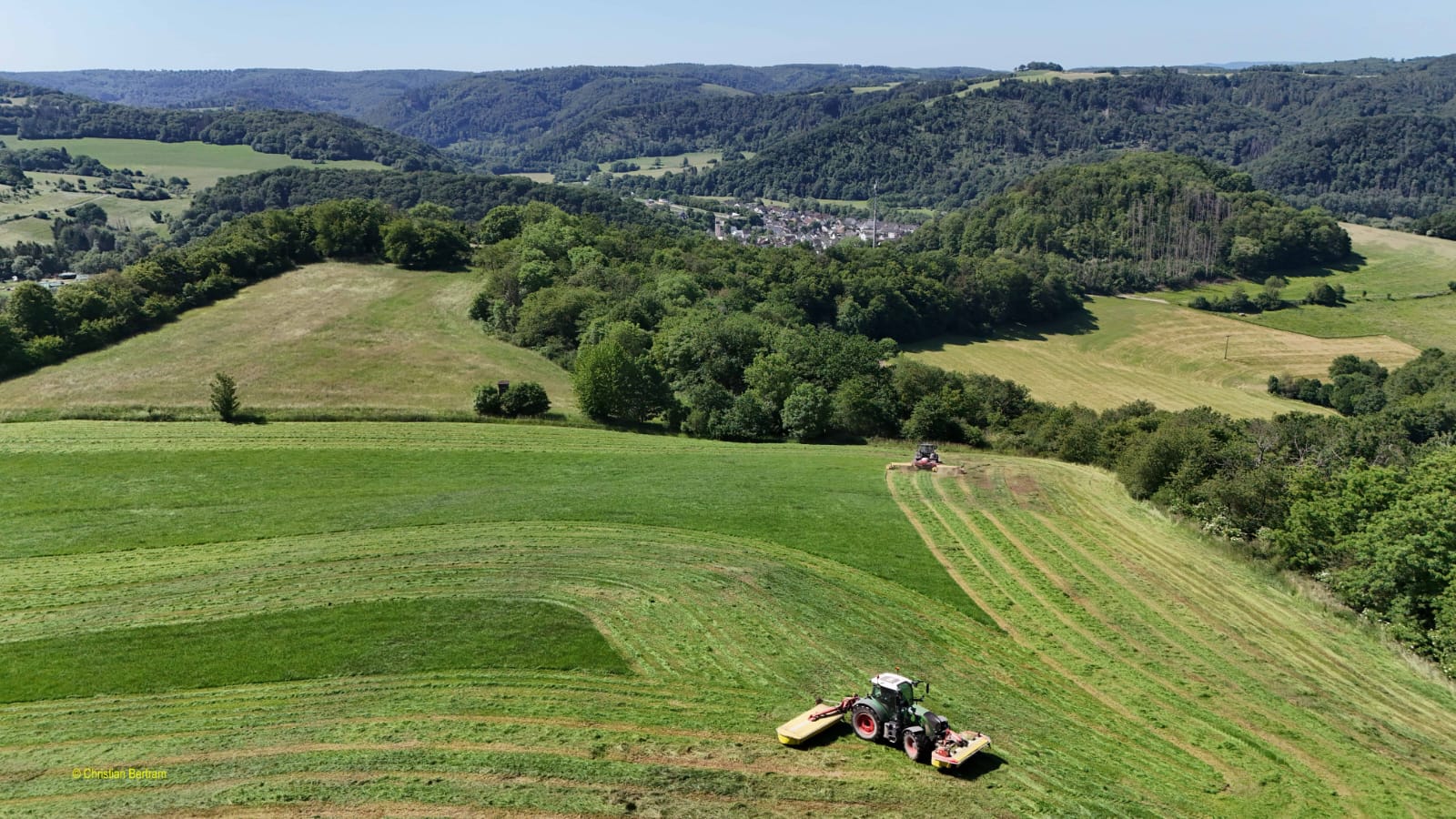 Luftaufnahme eines Talkessels mit Feldern, Wald und einem Dorf im Hintergrund